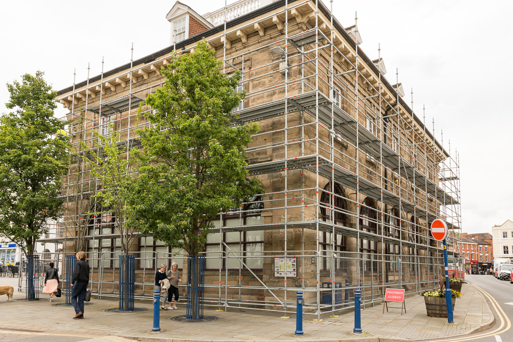 Partially erected scaffold on a high street in Warwick with heras fencing and footpath closed sign