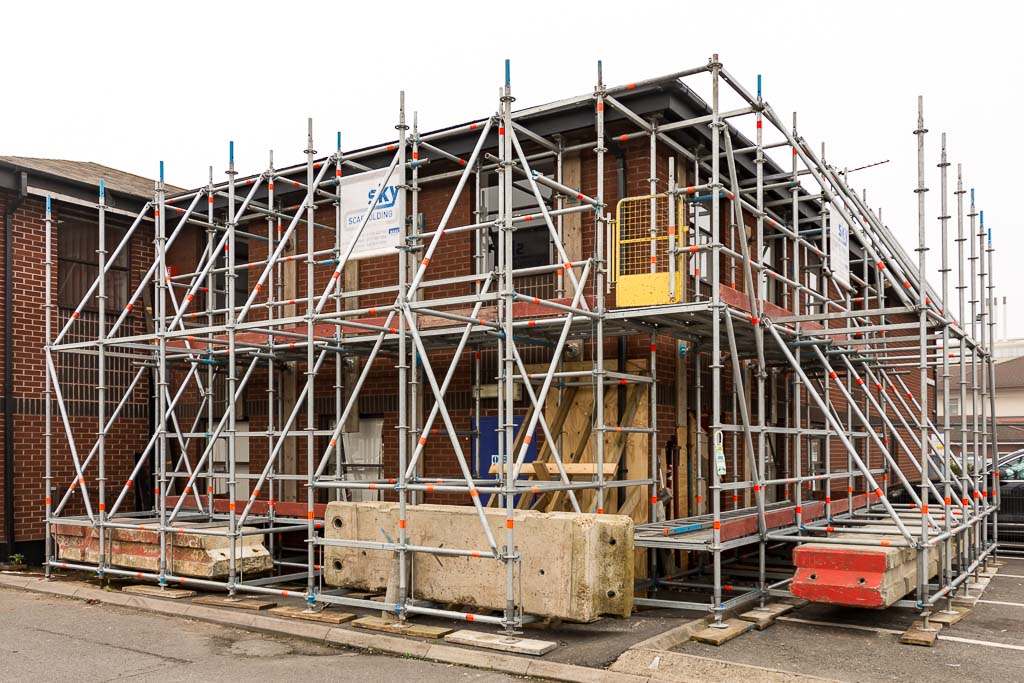 External support scaffold to two elevations of a brick building and the roof in a car park with concrete ballast