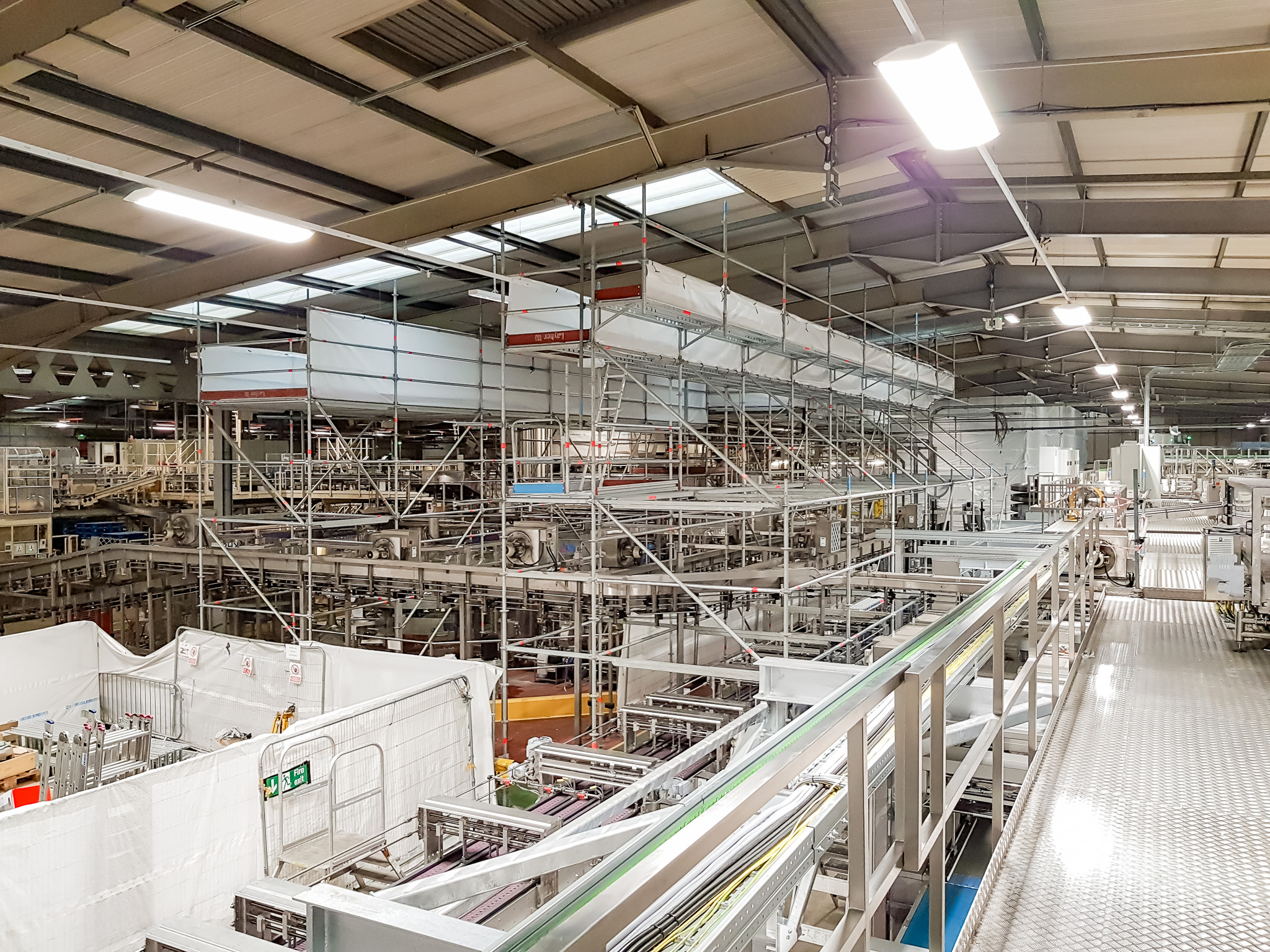 Free-standing scaffold structure to access lighting in a food and drink factory in Rugby. Erected in Layher system scaffold.